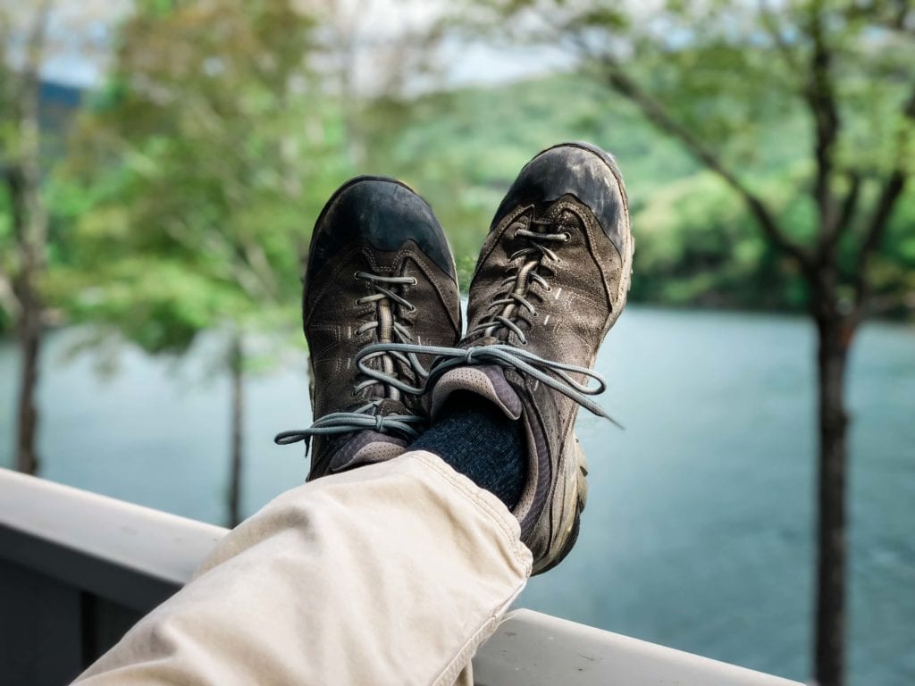 The wedding attire for the groom in an adventure elopement included his favorite scuffed and worn hiking shoes. Kicked up on the railing of the cabin , overlooking the lake while he waits for his partner to prepare for the ceremony.
