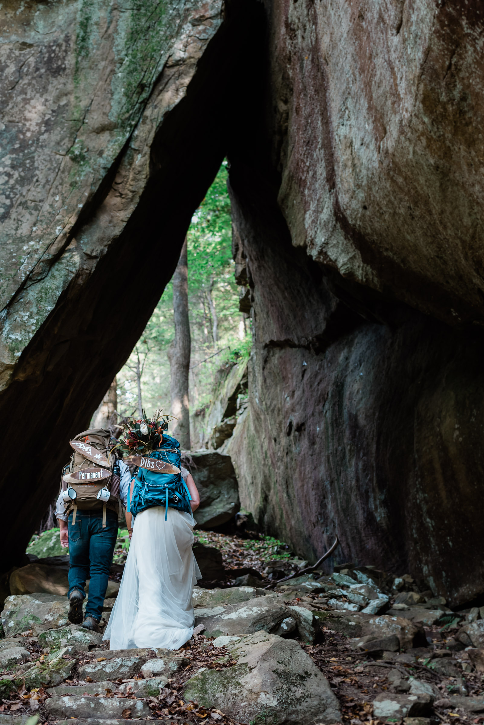 Hiking elopement with the bride and group walking under a natural stone arch in Kentucky with MAKE Adventure Stories Photography