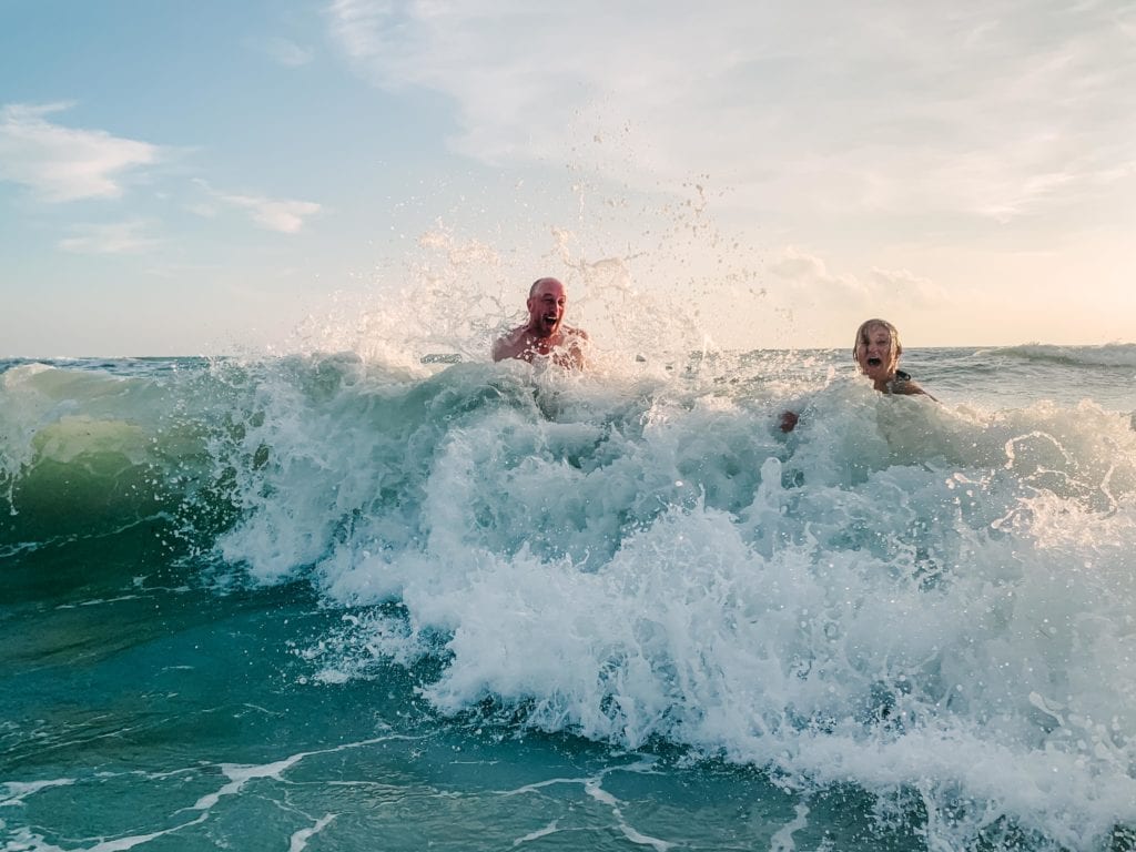 A couple playing and laughing as a wave hits them in the ocean by Charleston Elopement Photographer