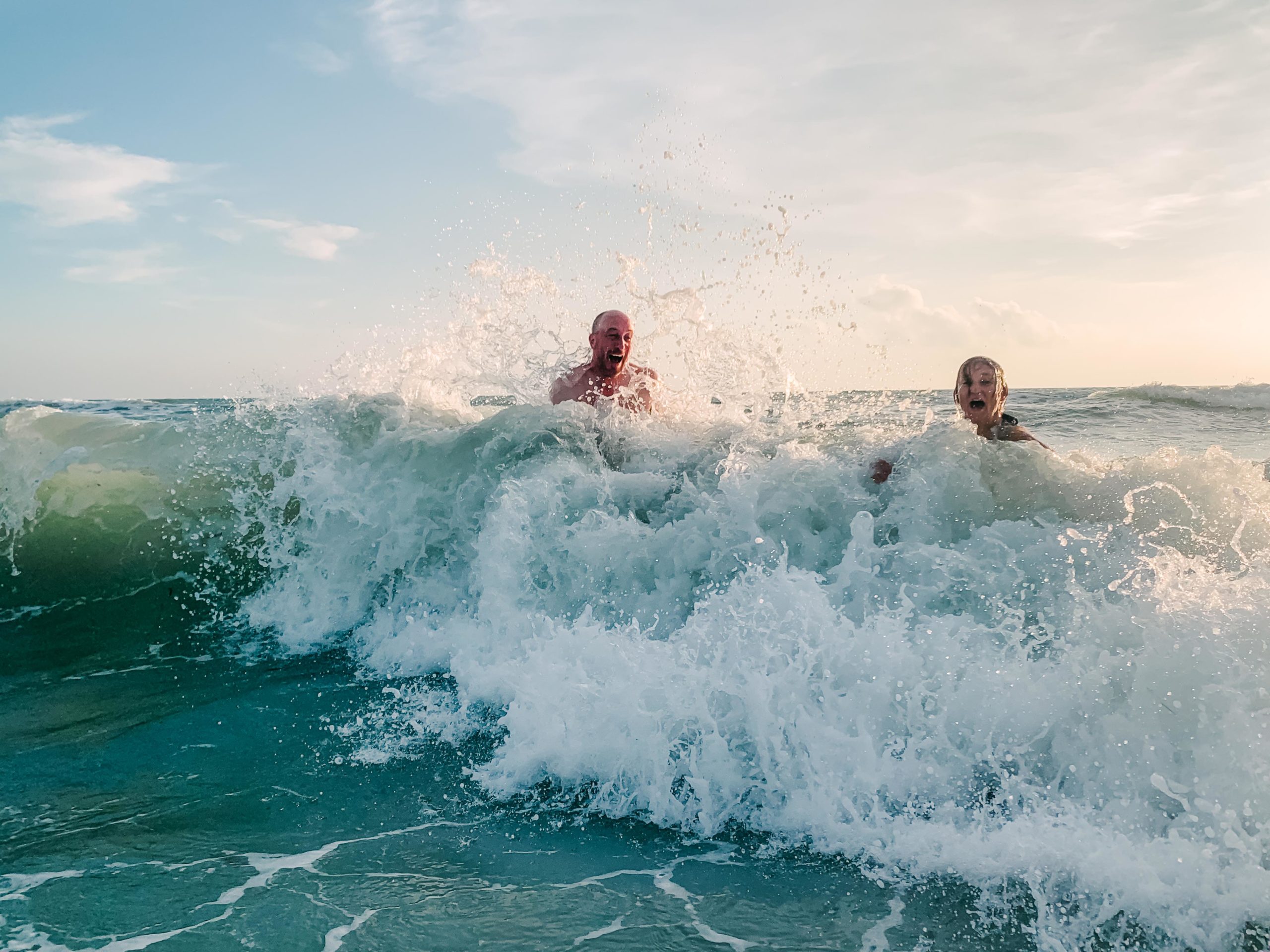 A couple playing and laughing as a wave hits them in the ocean by Charleston Elopement Photographer