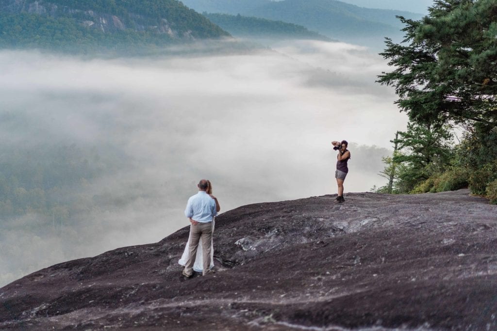 an adventure elopement photographer in the southeast captures a close up of a couple at the top of a cliff in North Carolina with rocks and trees and fog visible behind them
