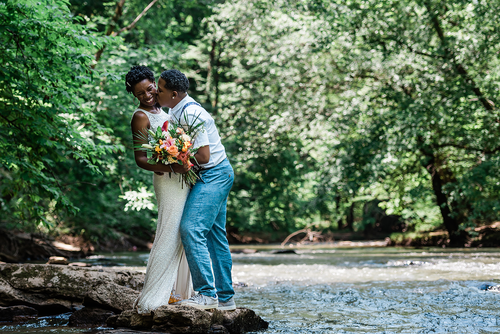 Partner gives his spouse a kiss on the cheek standing next to the creek at their adventure elopement