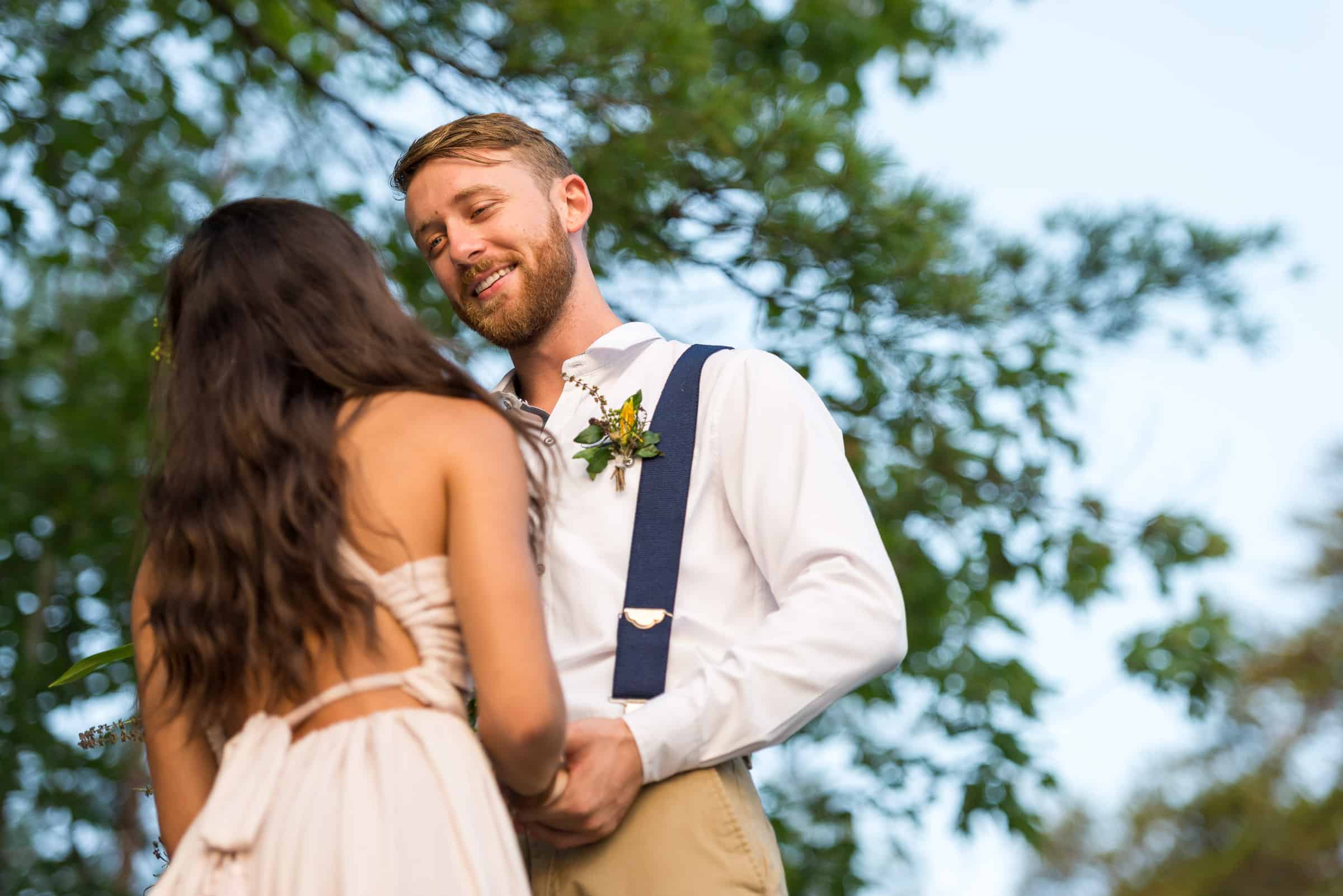 Groom looks down at bride, holding her hands and smiling. 