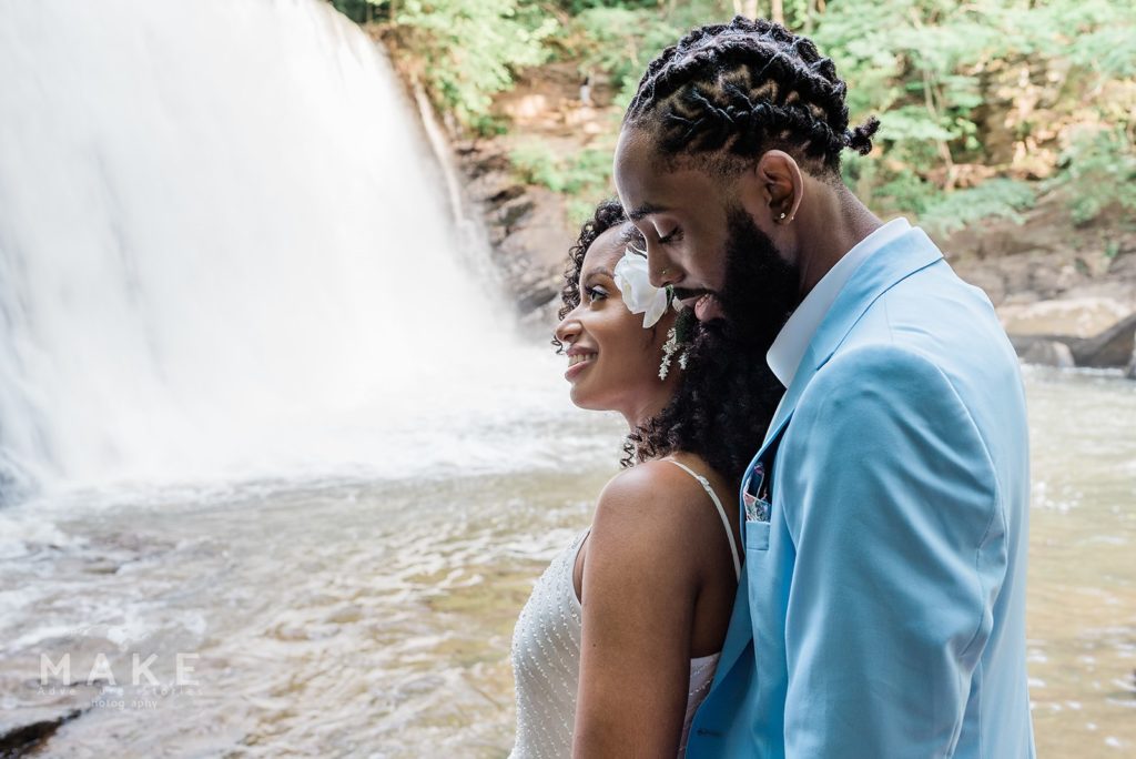 Couple stands looking off towards the waterfall at their elopement. This alternative to a courthouse wedding allowed them to exchange vows in a location special to them.