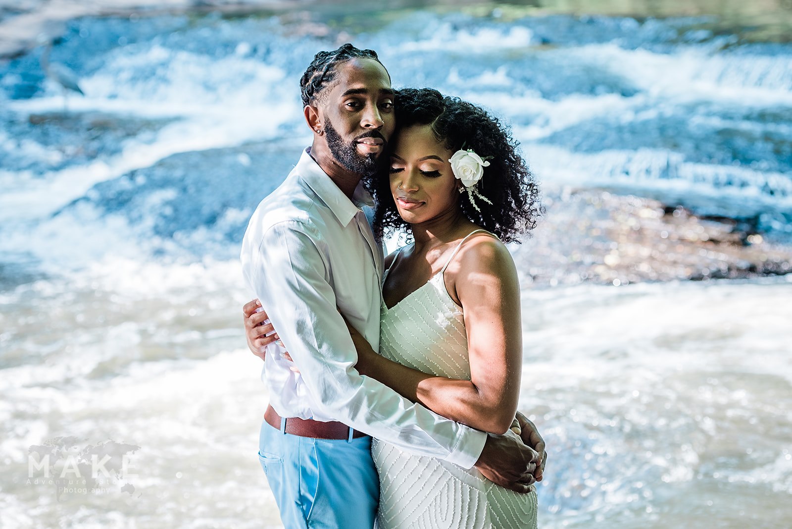 Couple embraces at the water's edge, groom looking at camera, during their adventure elopement (an alternative option to a courthouse wedding!). 