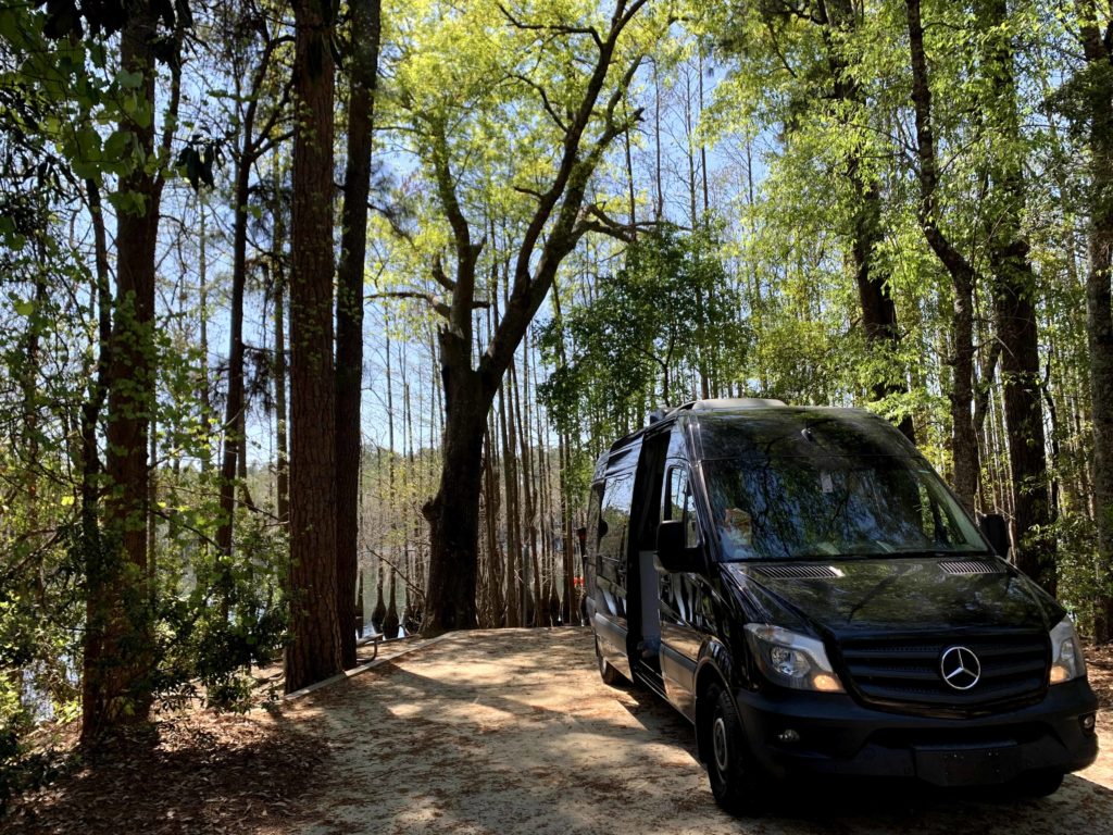 A black vanlife van rental used for a Georgia adventure elopement sits tucked into a beautiful grove of trees with water visible in the background