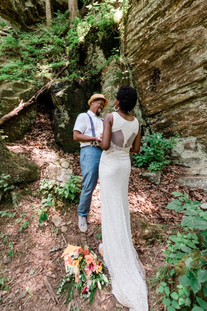 couple in wedding attire next to a cliff laughs during private vows whilefamily-helps-watch-young-kids-while-mom-and-dad-renew-their-vows-in-an-adventure-elopement-ceremony-3