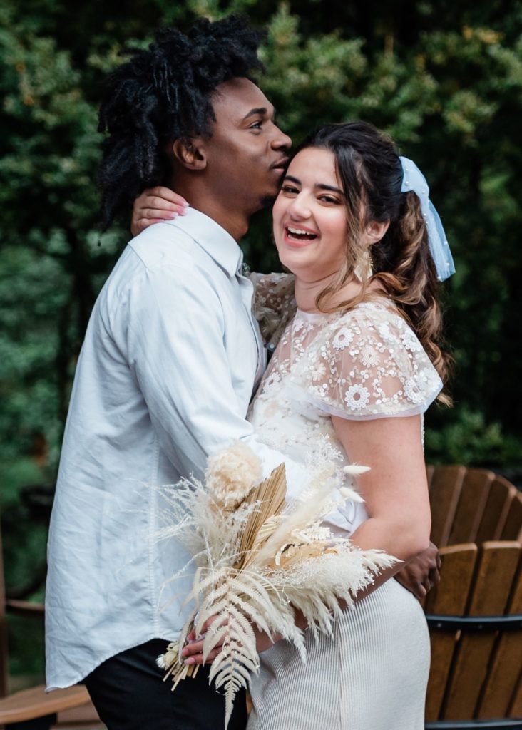 This is an image of a man and woman happy together after they shared their vows. The woman is looking at the camera laughing while the man is looking away leaning his face against hers. 