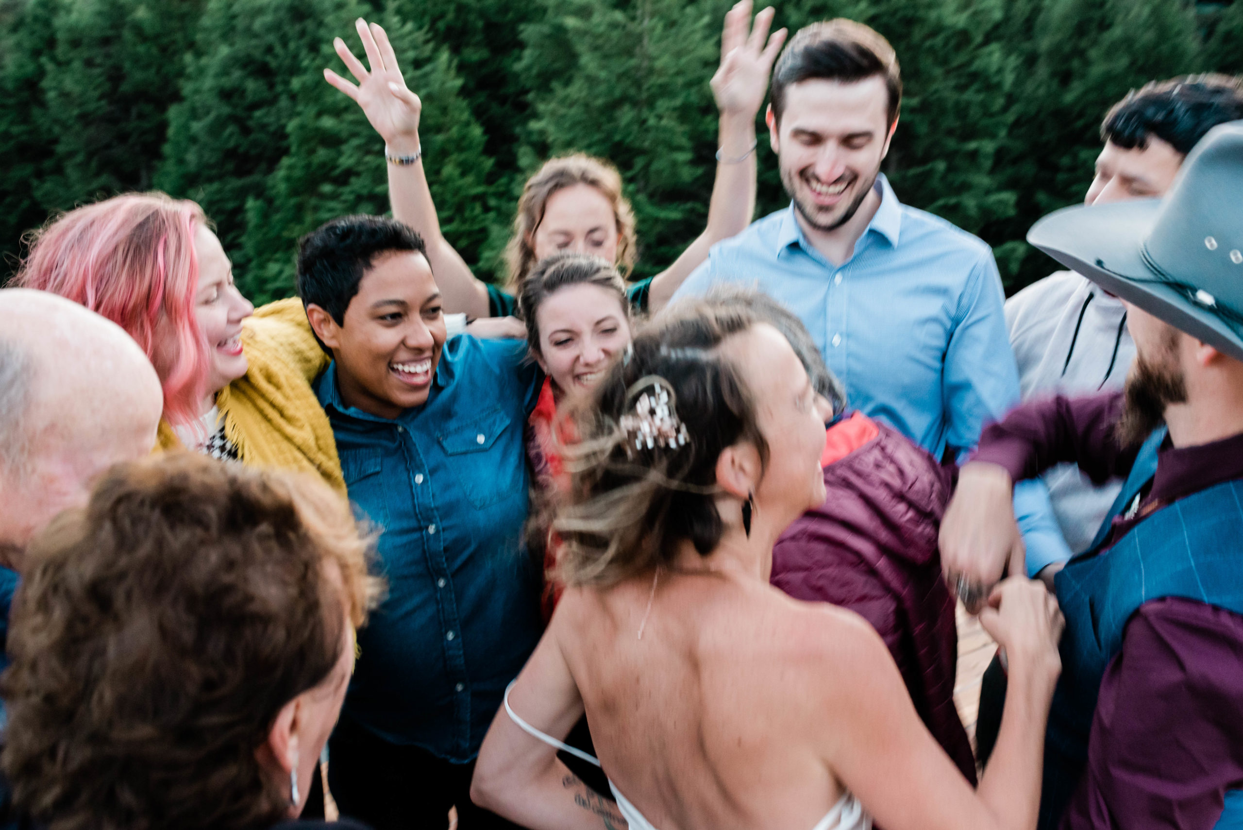 In this picture we see small wedding guest list. They are all dancing together in a circle. Everyone is smiling as the bride and groom dances with them.