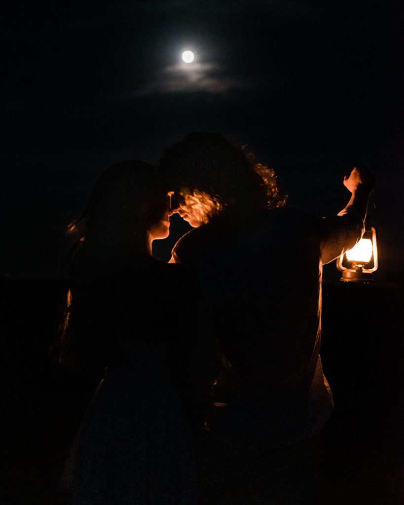 This is a picture taken at night of a couple holding a lantern and kissing. This elopement was a moon-light adventure.