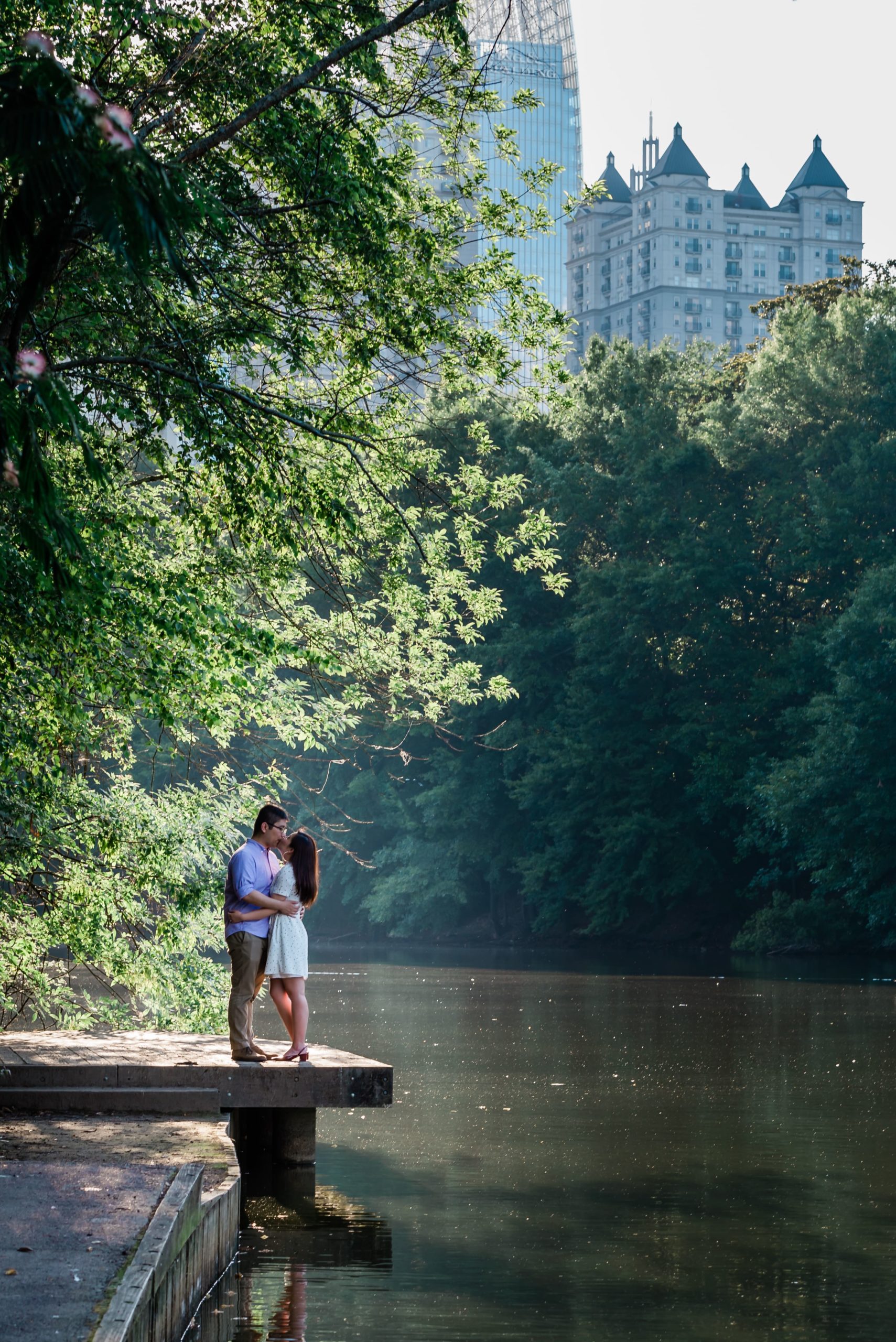 Taken in Piedmont Park, this portrait is by the water with the Atlants skyline in the back. A couple kisses on the dock.