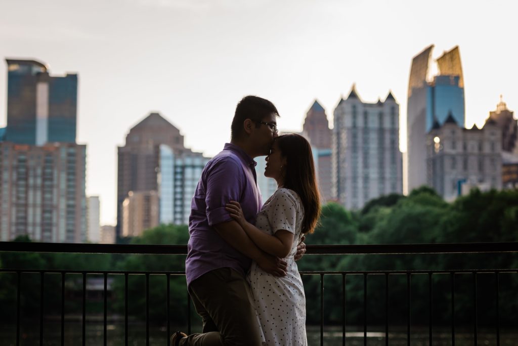 Taken in Piedmont Park, this portrait is by the water with the Atlants skyline in the back. A couple kising.