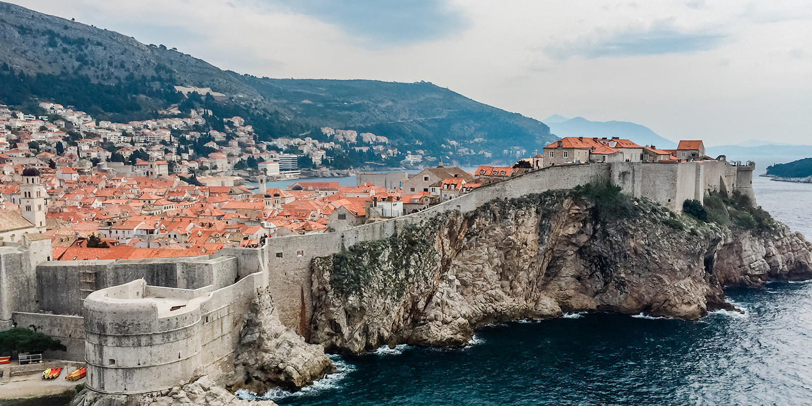 Adventure Wedding Photography can happen anywhere, including Croatia! This picture if of a Croatian cliff side city. You can see the ocean, the mountains, and the warm orange roofs of the buildings.