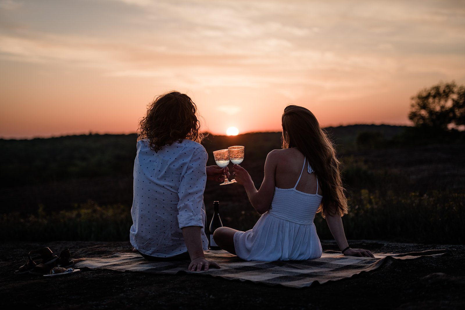 This is a picture of an engaged couple during their sunset engagement photos. They are cheering champagne as the sunsets