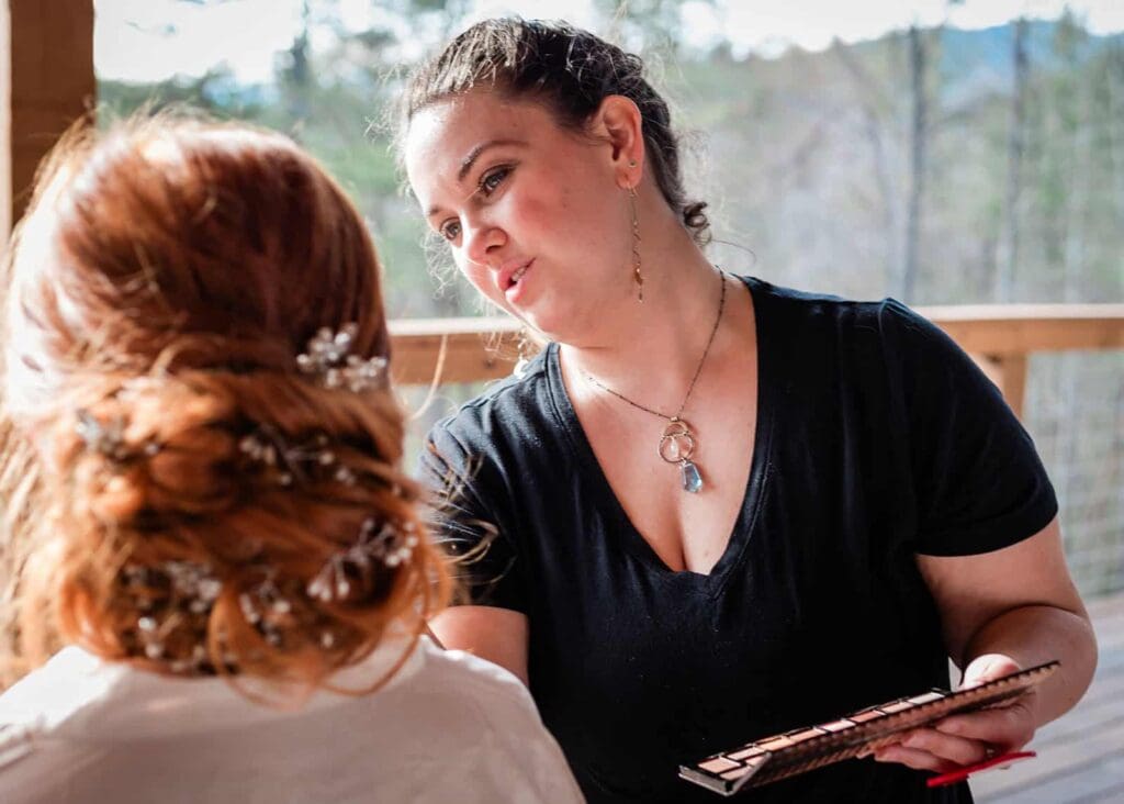 a hair and makeup artist applies makeup to a bride with red hair at a remote microwedding as a part of the trusted vendor team