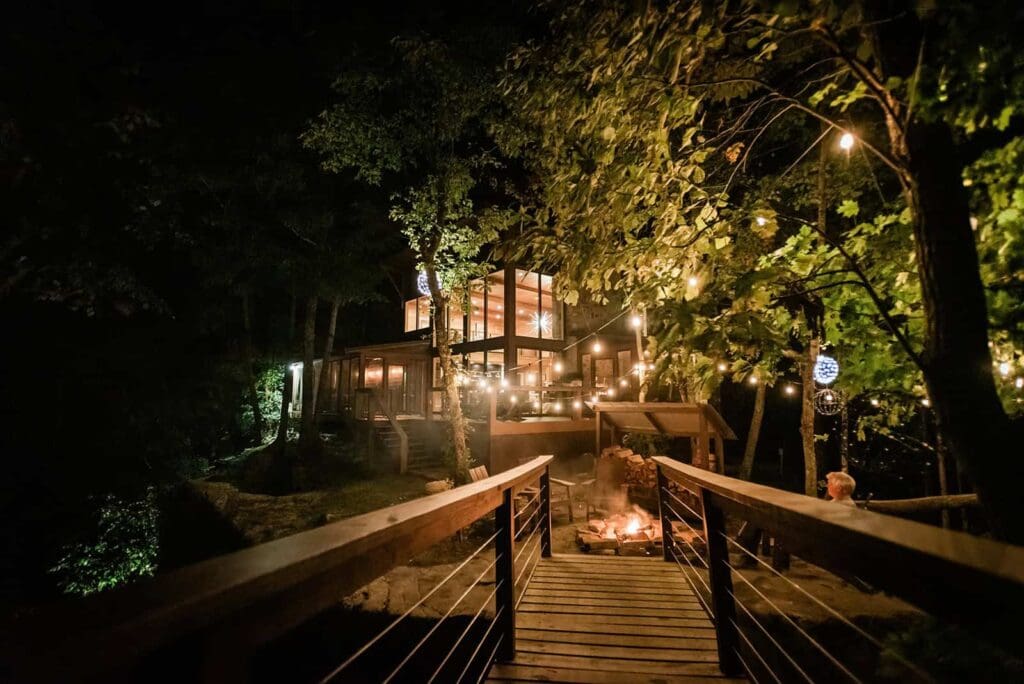 The large modern cabin called Top of the Rock at The TreeLofts property in Tennessee is all lit up at night in a golden glow with a campfire in the foreground ready for an adventure elopement wrap up.